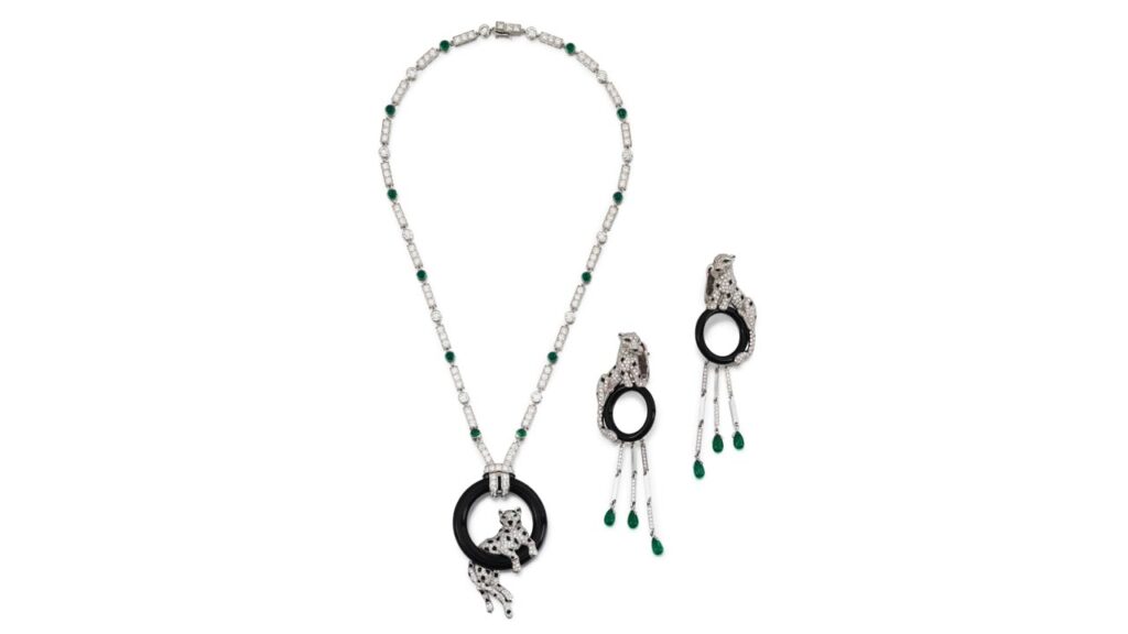 Cartier jewels, this one a demi-parure comprising a pendant necklace featuring a panther pavé-set with brilliant-cut diamonds and decorated with pear-shaped emerald eyes and an onyx nose and spots. The panther is resting inside an onyx hoop, which suspends from a chain with cabochon emeralds and brilliant-cut diamonds. It comes with matching earrings at Sotheby's image