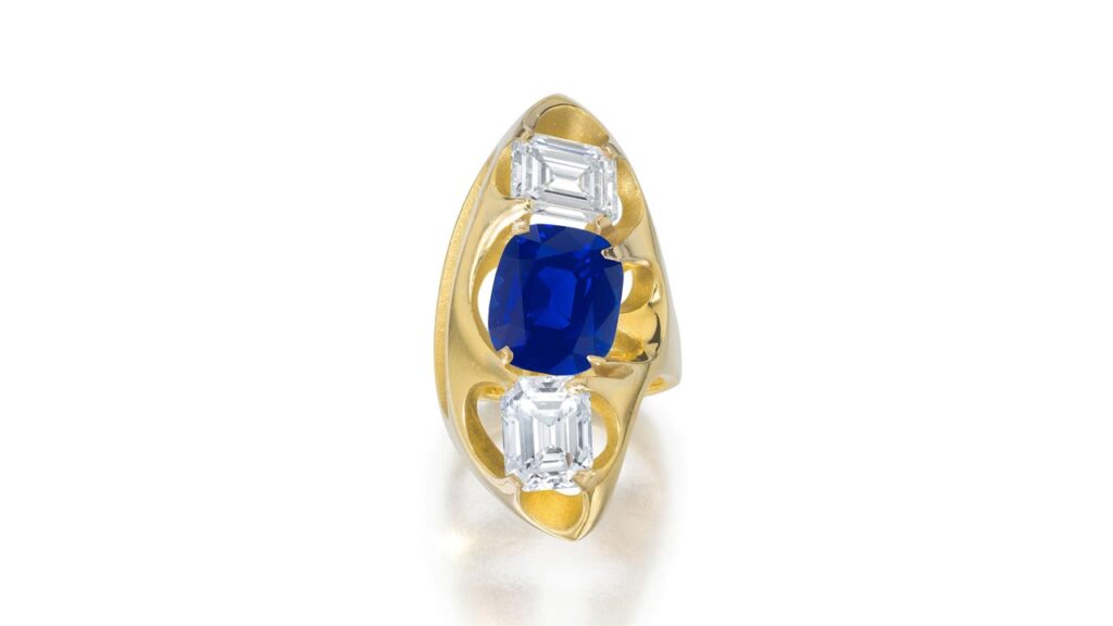 A ring bearing a cushion-shaped, 6.92-carat, royal-blue Kashmir sapphire within an openwork mount accented with two emerald-cut, 2.34- and 2.62-carat diamonds at Bonhams image