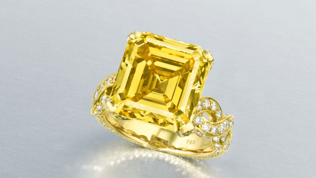 A ring bearing an emerald-cut, 10.39-carat, fancy-vivid-yellow, VVS1 diamond with round diamonds on the band at Christie's image