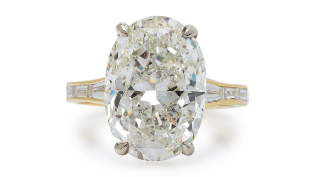 This ring features an oval modified brilliant-cut, 10.02-carat, K, SI1 diamond, a circle of round diamonds around the prong setting, and baguette-cut diamonds lining the shank and band at Freeman's image