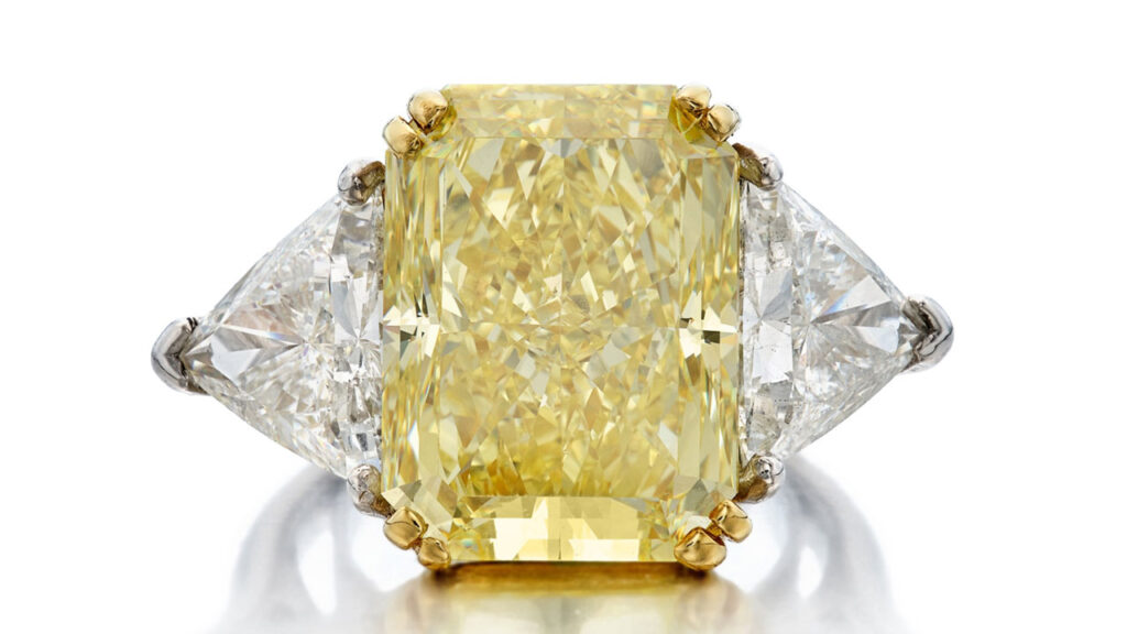 A cut-cornered rectangular mixed-cut, 14.22-carat, fancy-intense-yellow, VS1 diamond is the star of this ring, sitting between two triangle-shaped diamonds at Sotheby's image
