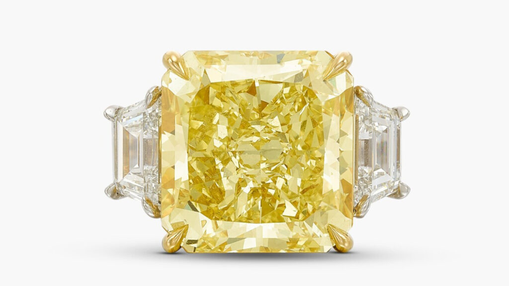 A ring starring a radiant-cut, 10.22-carat, fancy-intense-yellow, VVS1 diamond between two trapeze-shaped stones at Sotheby's image
