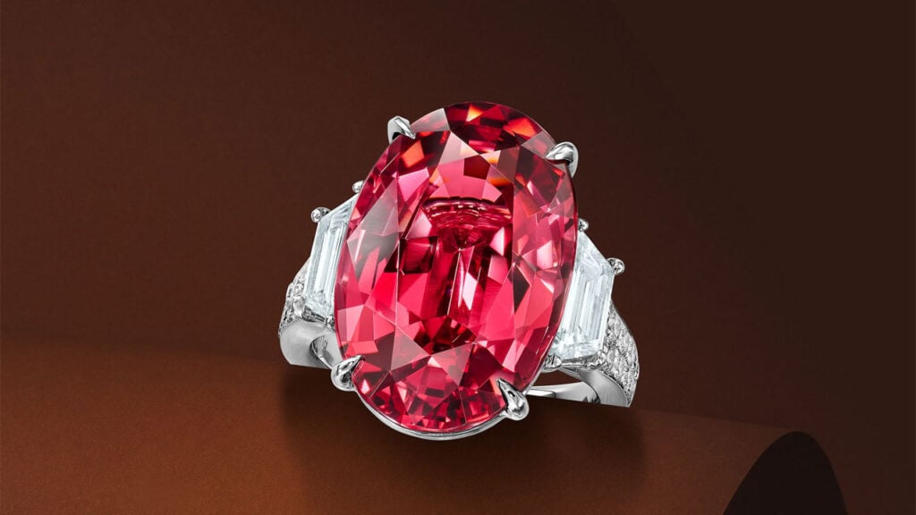 A ring centering an oval, 16.50-carat, pinkish-red Tanzanian spinel between two tapered baguette-cut diamonds, with round brilliant-cut diamond shoulders at Bonhams image