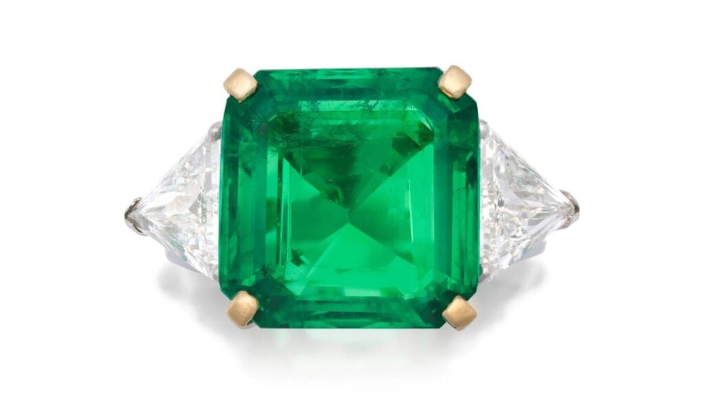 This ring bears an octagonal step-cut, 9.13-carat Colombian emerald flanked by two trilliant-cut diamonds. at Bonhams image