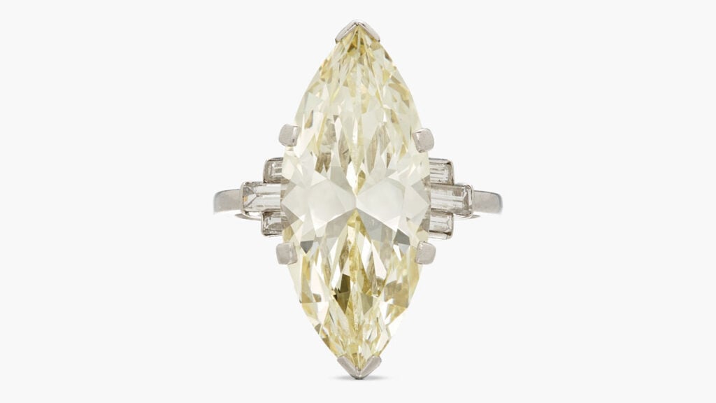 A ring with a marquise-shaped, 9.19-carat, fancy-yellow, VS1 diamond, between baguette diamonds at Sotheby's image