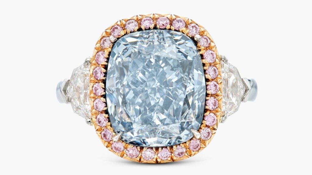 A ring with a cushion modified brilliant-cut, 6.76-carat, fancy-greyish-blue, SI1 diamond center stone, in a pink-hued round-diamond surround, between shield-shaped diamonds at Sotheby's image