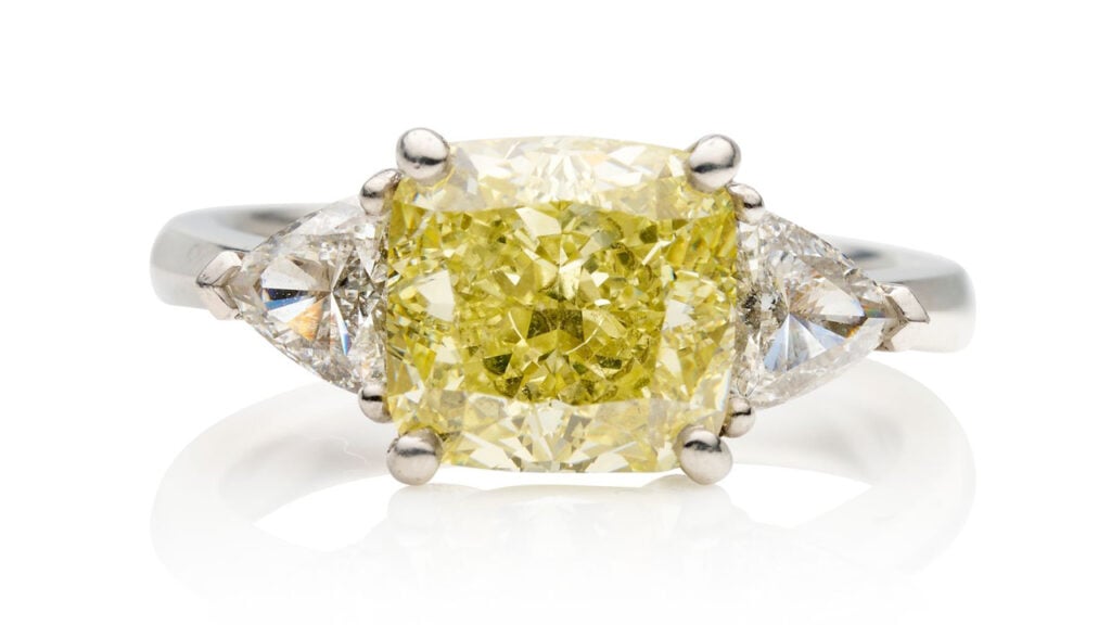 This ring features a cushion-shaped, 4.07-carat, fancy-intense-yellow, VVS1 diamond between trilliant-cut stones at Bonhams image