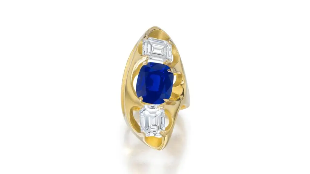 A ring bearing a cushion-shaped, 6.92-carat, royal-blue Kashmir sapphire within an openwork mount accented with two emerald-cut, 2.34- and 2.62-carat diamonds at Bonhams image