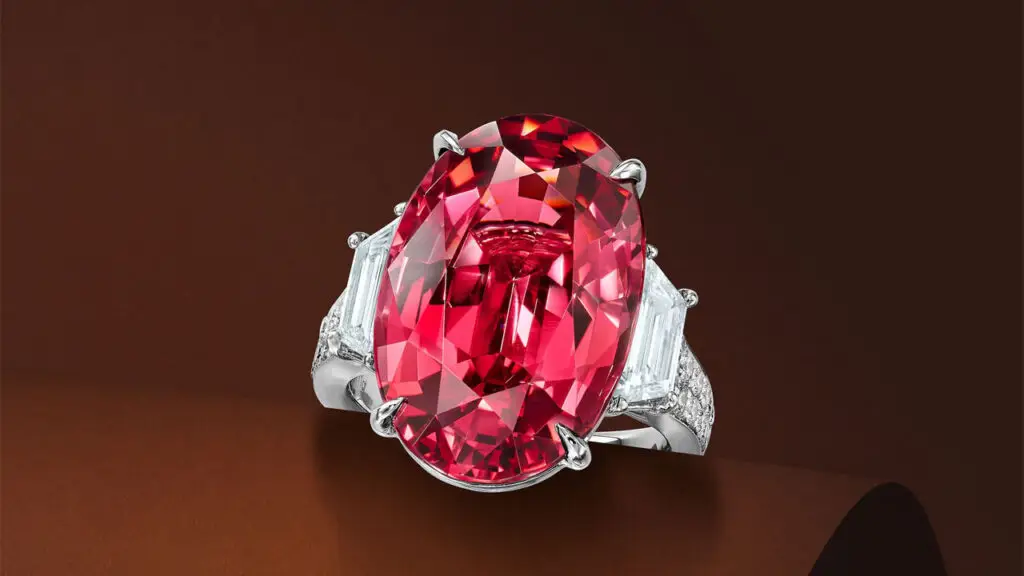 A ring centering an oval, 16.50-carat, pinkish-red Tanzanian spinel between two tapered baguette-cut diamonds, with round brilliant-cut diamond shoulders at Bonhams image