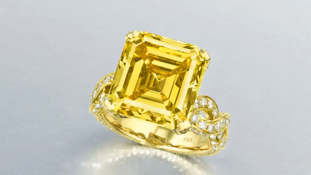 A ring bearing an emerald-cut, 10.39-carat, fancy-vivid-yellow, VVS1 diamond with round diamonds on the band at Christie's image