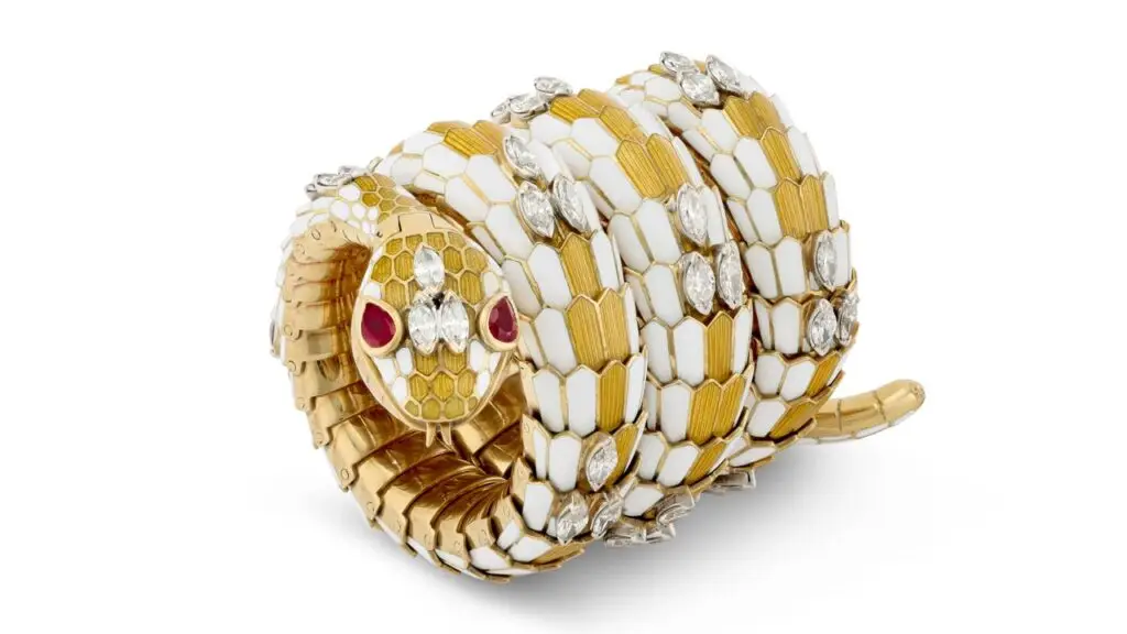 A Bulgari bracelet-watch is designed as a serpent. It has yellow and white enamel, marquise-shaped diamonds, and pear-shaped rubies as eyes at Christie's image