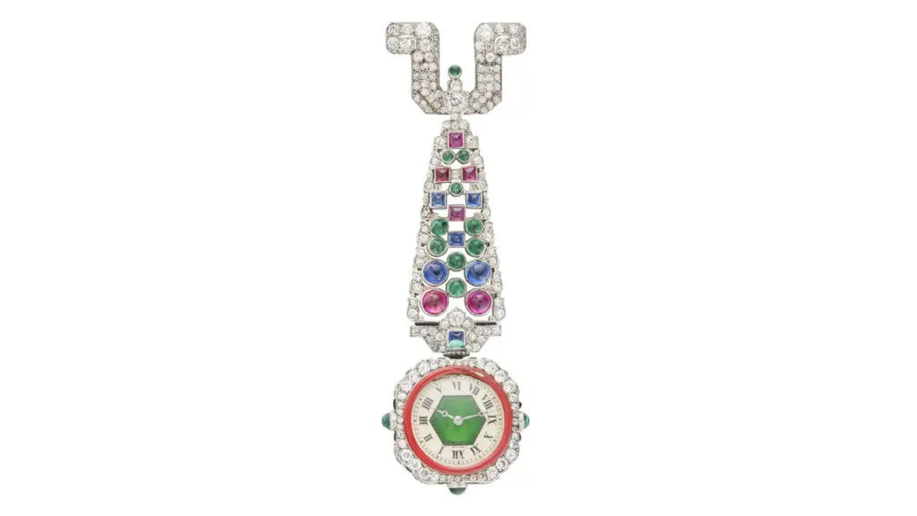 An Art Deco-designed Cartier piece from around 1925 features a watch face in a round-diamond surround, suspended from old- and single-cut diamonds, round and sugarloaf cabochon sapphires, rubies, emeralds, ring-shaped pierced emerald, red enamel, plaque and sugarloaf cabochon onyx Christie's image