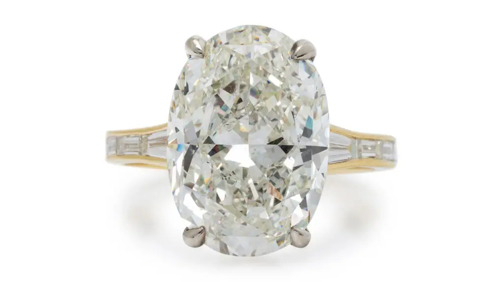 This ring features an oval modified brilliant-cut, 10.02-carat, K, SI1 diamond, a circle of round diamonds around the prong setting, and baguette-cut diamonds lining the shank and band at Freeman's image