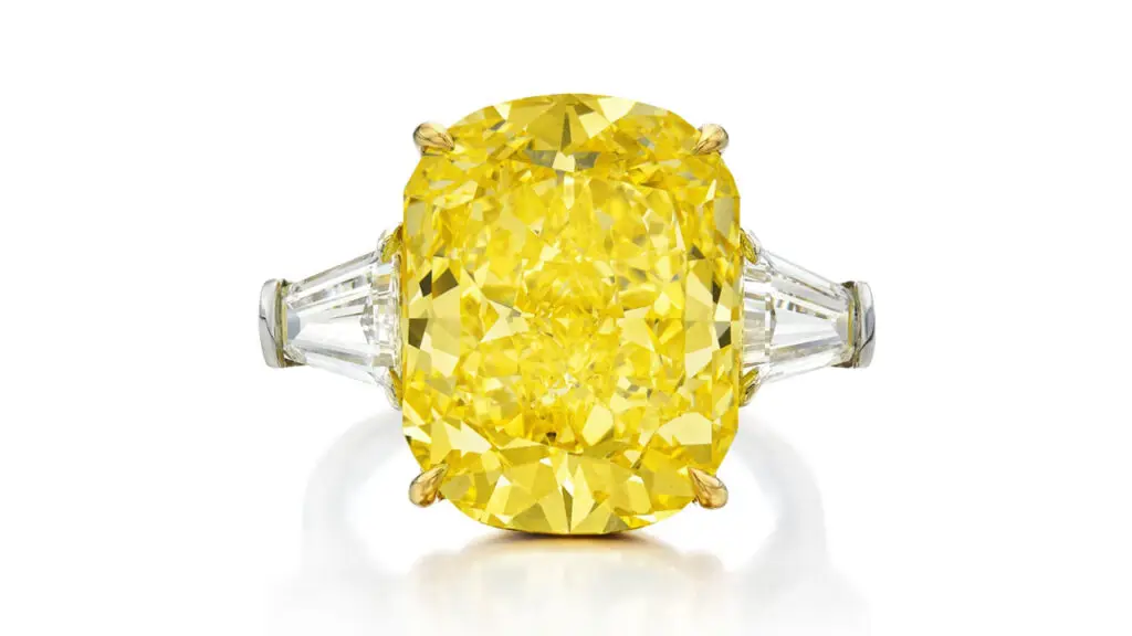 Bulgari ring bears a round-cornered rectangular modified brilliant-cut, 12.51-carat, fancy-vivid-yellow, internally flawless diamond between two tapered baguette diamonds at Sotheby's image