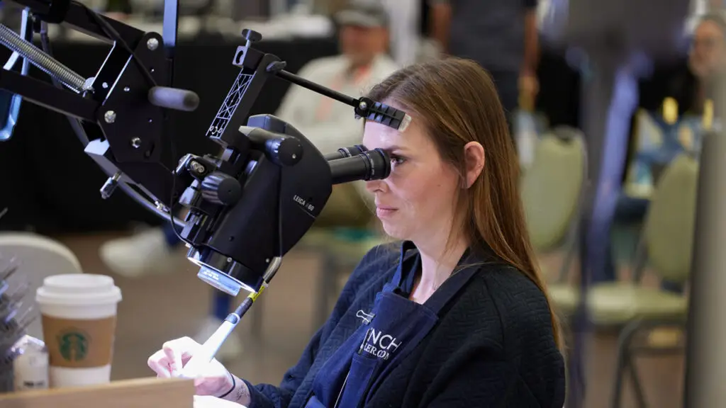 A woman views gems under a microscope at a bench event with the Women’s Jewelry Association (WJA) image