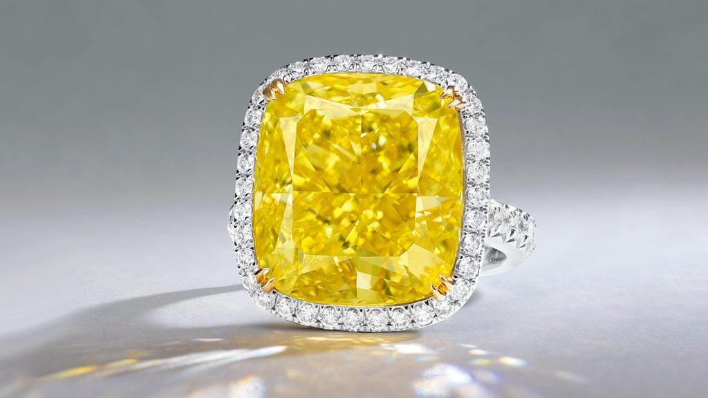 A ring bearing a cushion-cut, 15.81-carat, fancy-intense-yellow, VS2 diamond, embellished with circular-cut diamonds at Poly Auction image
