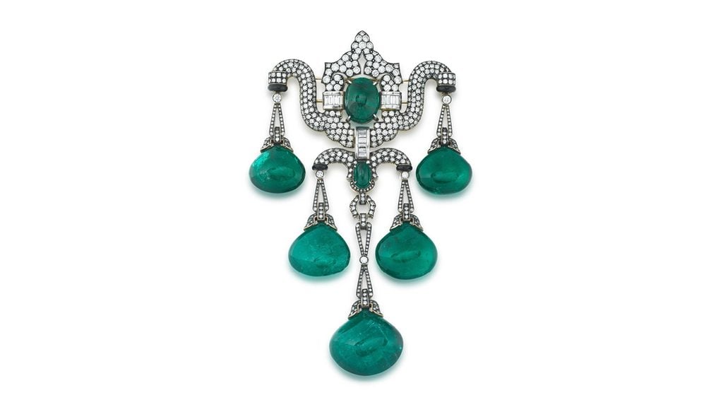 A brooch designed as an articulate swag, sporting cabochon emerald drops accented with onyx. The mount features an oval emerald cabochon and is pavé-set with brilliant- and baguette-cut diamonds. The emeralds are of Zambian origin and total 172.50 carats at Sotheby's image