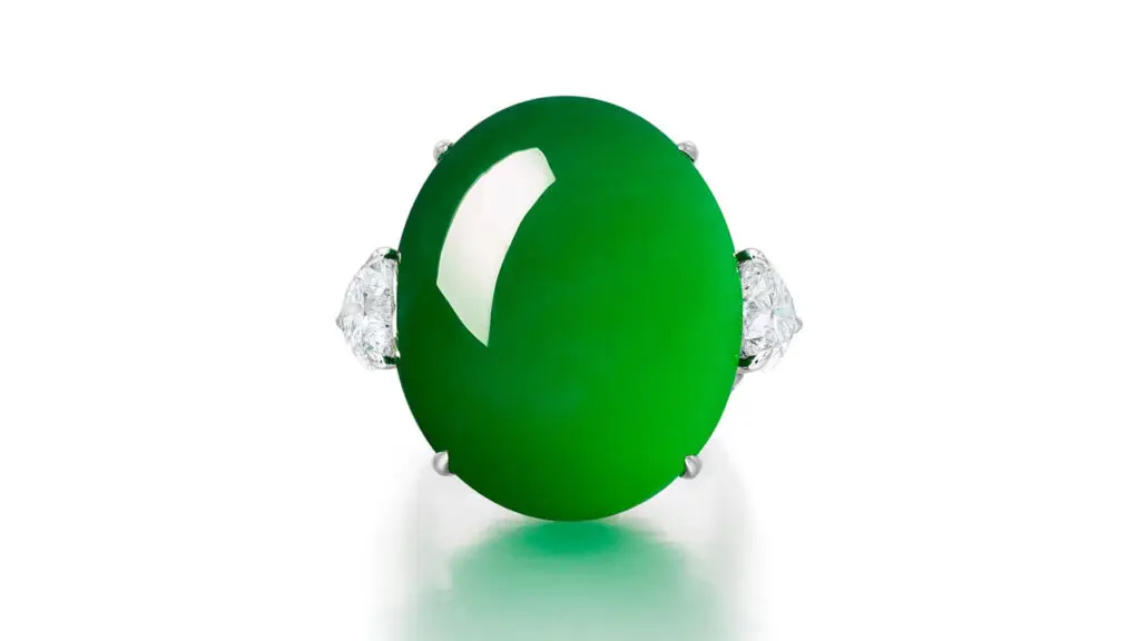 An oval jadeite cabochon ring of bright-green color, accented by two heart-shaped and brilliant-cut diamonds at Sotheby's image