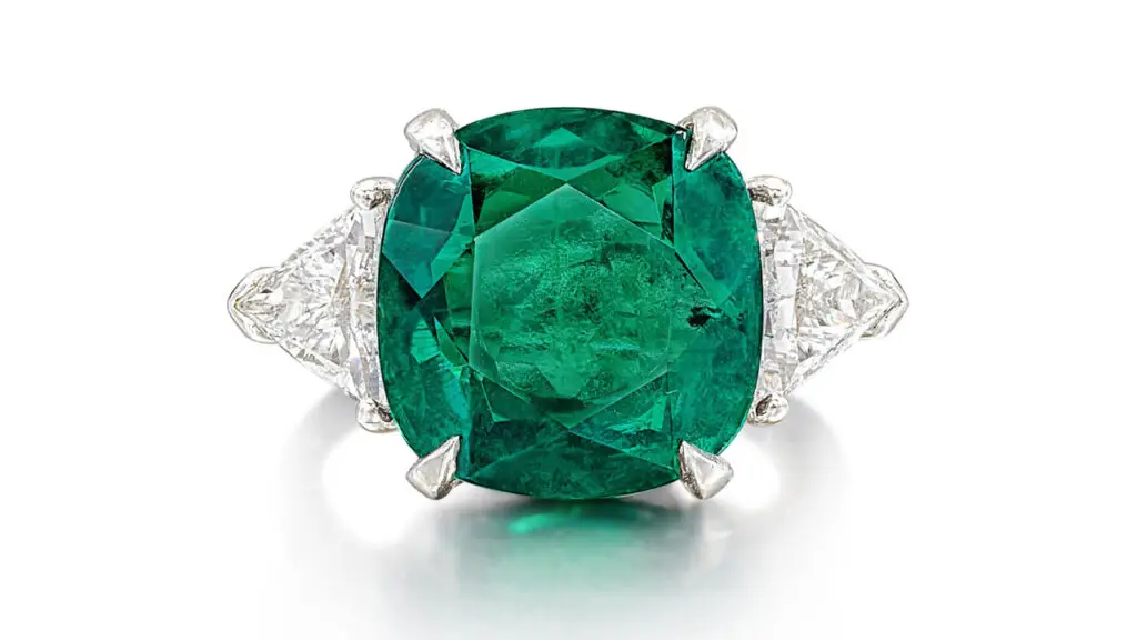 A ring featuring a cushion-shaped, 10.02-carat Colombian emerald between two triangular diamonds at Sotheby's image