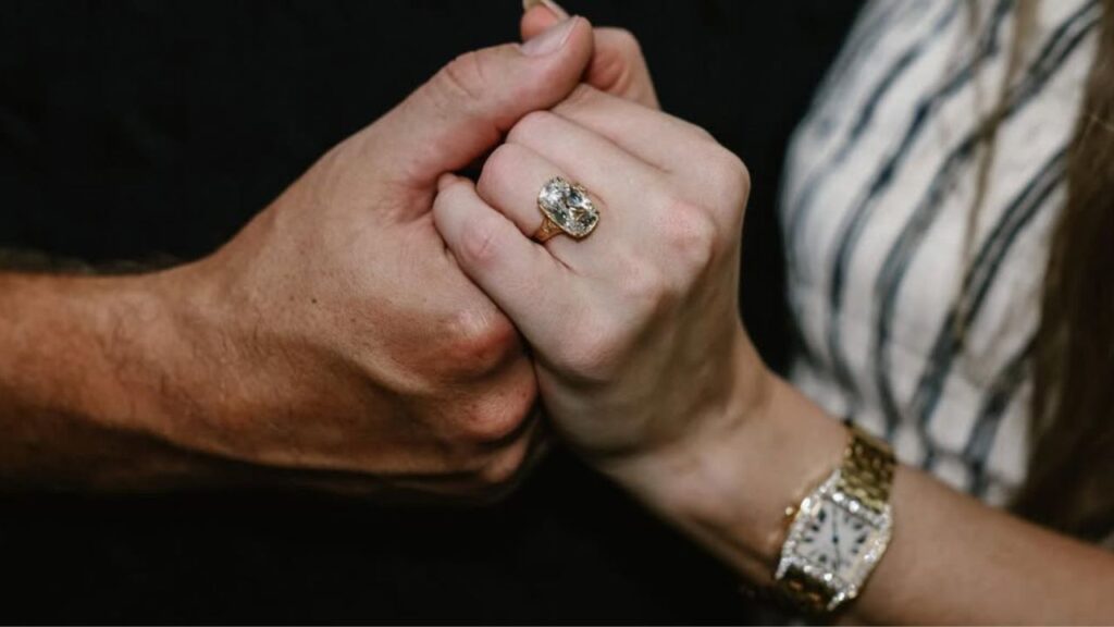 Taylor Swift holding Travis Kelce's hand, displaying her diamond engagement ring image