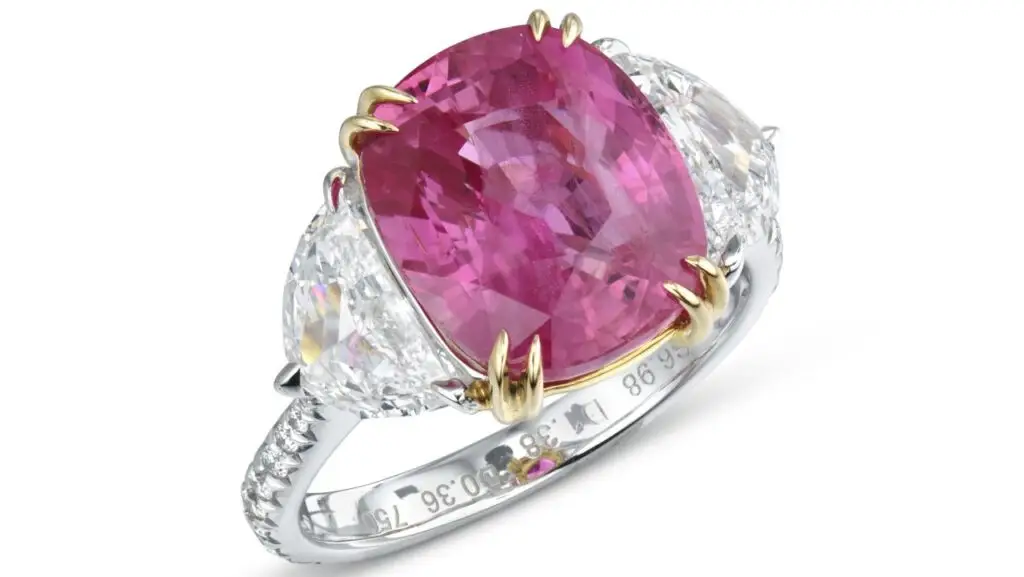 A ring centering a cushion-shaped, 6.99-carat Madagascar padparadscha sapphire between two half-moon diamonds, with round diamonds on the band at Christie's image