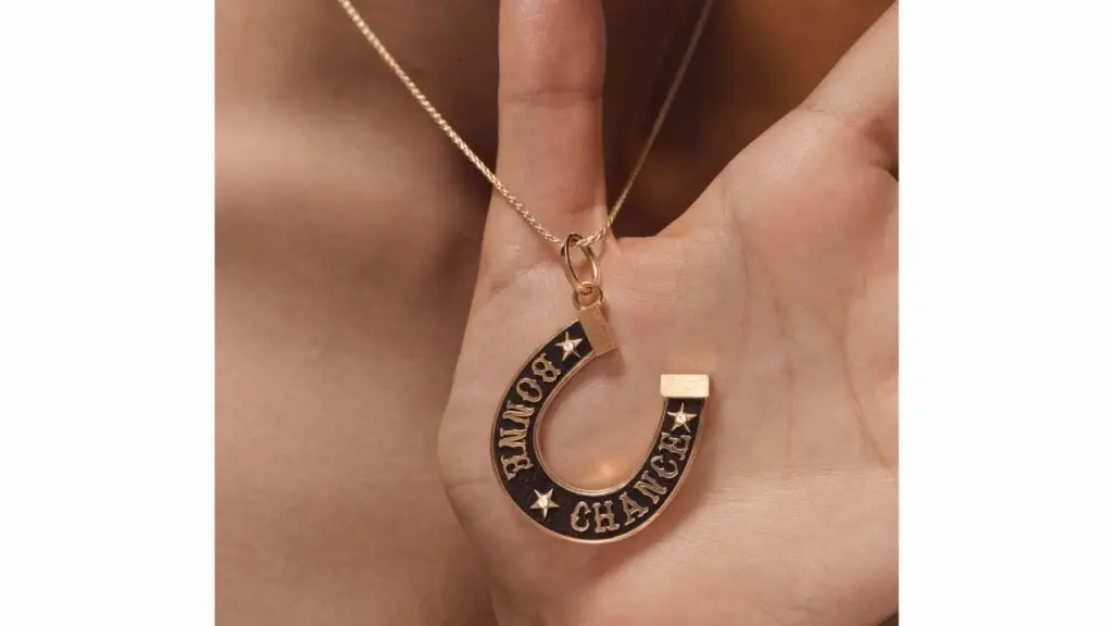 A horseshoe-shaped Marie Lichtenberg pendant with the words Bonne Chance in 18-karat gold and diamonds on wood image
