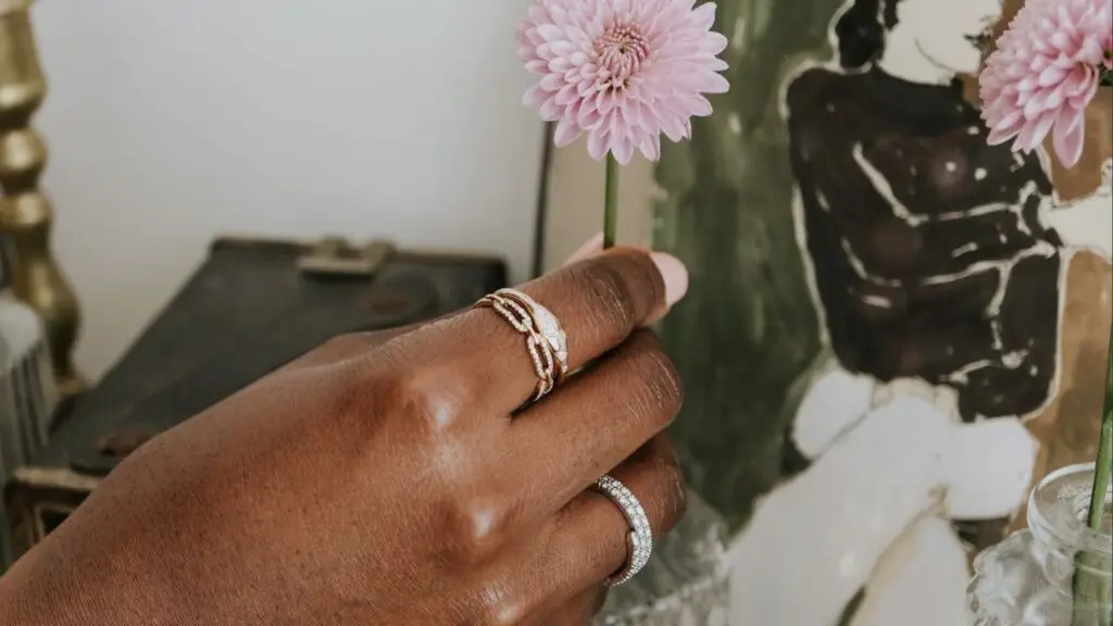 A model holds a flower while wearing gold and diamond rings available at Day’s Jewelers image