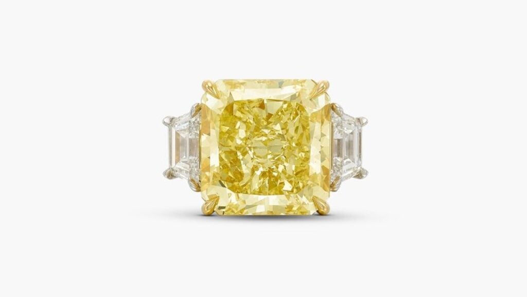 A ring offered with no reserve features a radiant-cut, 10.22-carat, fancy-intense-yellow, VVS1 diamond between two trapeze-shaped stones at Sotheby's image
