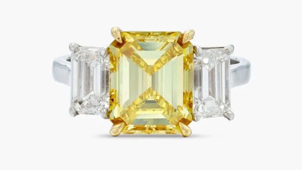 A ring centering an emerald-cut, 4.20-carat, fancy-vivid-yellow, VVS2-clarity diamond between two emerald-cut diamonds of 1.07 and 1.08 carats at Sotheby's image